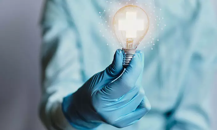 Nurse in scrubs holding a lightbulb to signify innovation
