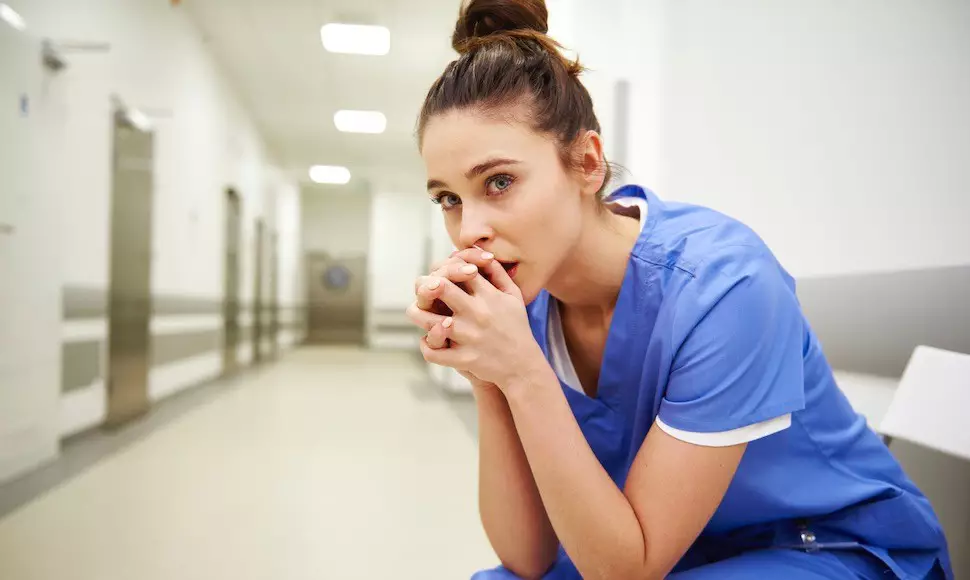 Nurse sitting with her hands in her  hands together, looking worried