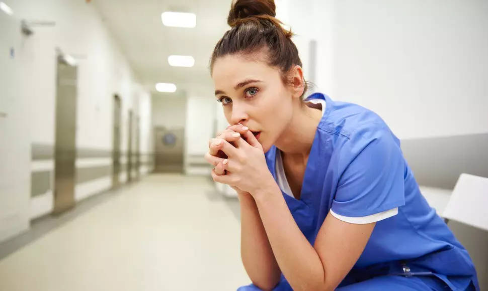 Nurse sitting with her hands in her hands together, looking worried and stressed like she could be suffering from nurse burnout.