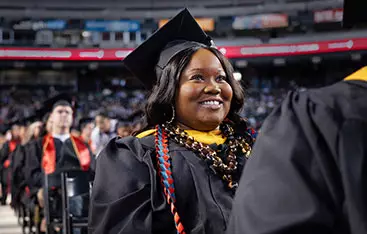 A happy ɫƵ graduate smiles into the crowd at a commencement ceremony