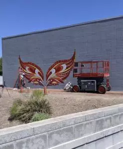 Artist Kelsey Montague paints a mural of phoenix wings on the campus building
