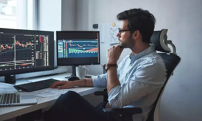 Man overlooking his two monitors as he wrangles data