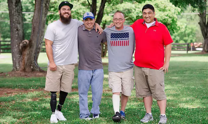 Four men stand smiling in the yard of the Willing Warriors retreat