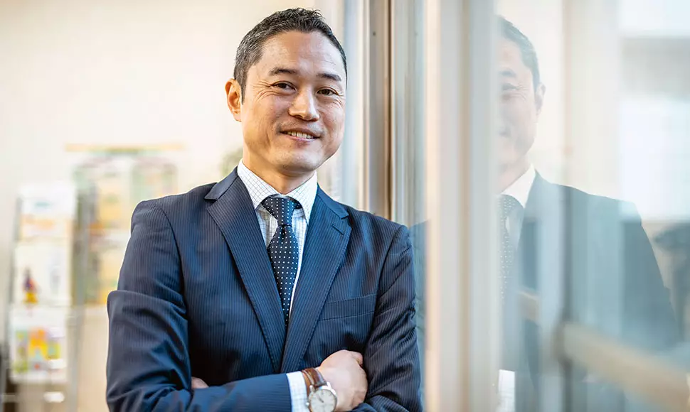Image of a confident, smiling business leader leaning against a pane of glass.