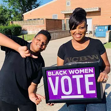 Tammie Otukwu and her son hold a sign outside encouraging Black women to vote