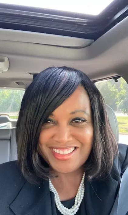 Tammie Otukwu smiles in the car while wearing a black suit and pearls