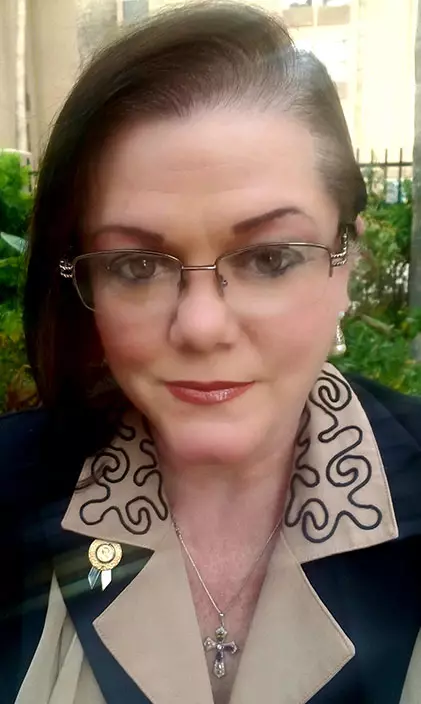 Tracylyn Sharrit stands outside wearing a blouse and glasses