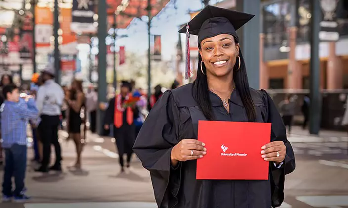 Female graduate smiling in cap and gown with diploma