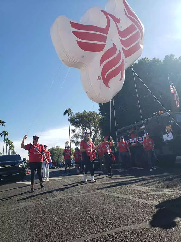 University of Phoenix volunteers walking in the 2024 Veterans Day Parade and holding a large phoenix float representing the University.