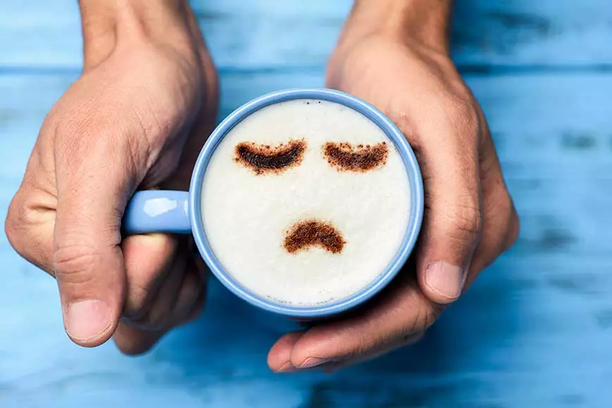 A coffee drink with a frowning face shown on it in coffee foam to signify workplace burnout