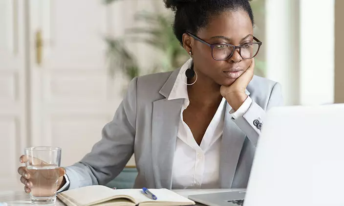 Business woman looking at her laptop with a notebook in front of her