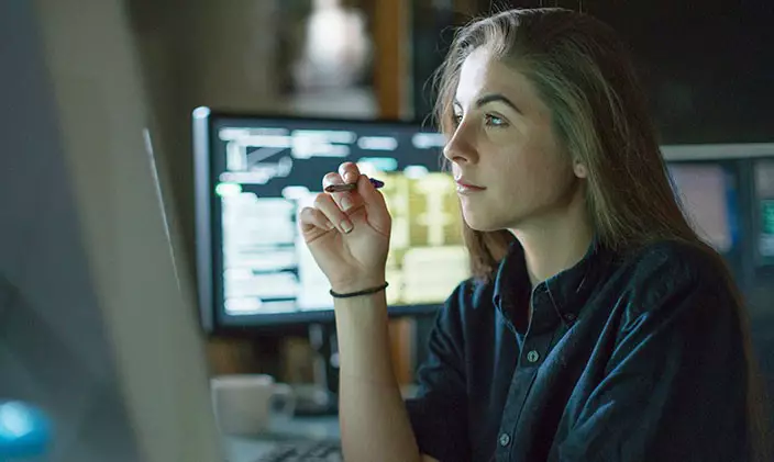Profile of a woman staring into a computer screen, surrounded by the soft glow of monitor light