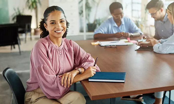 Young woman of color smiles while co-workers collaborate in the background